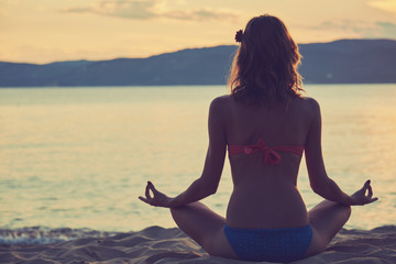 Fototapeta na wymiar Young woman practicing yoga on the sandy beach.