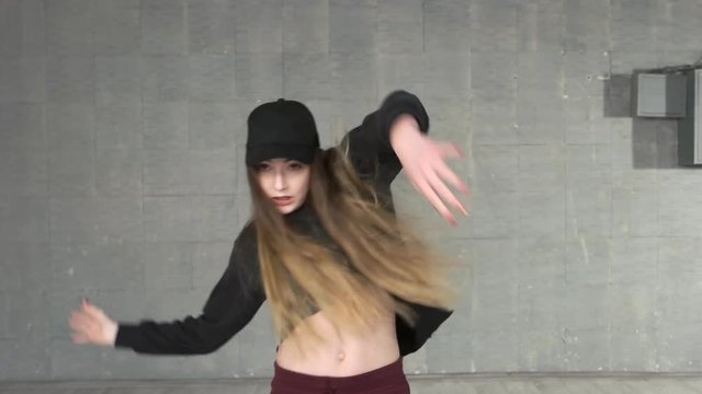 Pretty teenage girl practicing dance moves. Young beautiful slim girl dancing on a grey studio background.