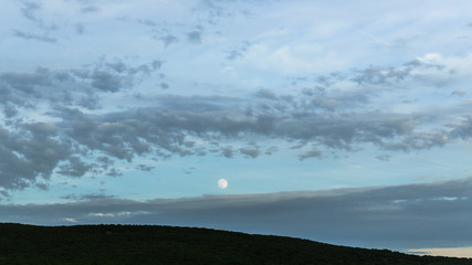 Moon rise in cloudy sky over mountains