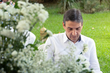 Happy groom with a linen white guayabera on his wedding day. Groom´s boutonniere. Happy and thoughtful man getting ready to get married. Casual style groom wear for wedding.