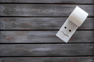 Toilet paper roll with painted face for proctology diseases concept on wooden background top view mock-up