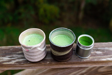 Wooden railing on backyard deck garden and two cups with Japanese vibrant green tea matcha foam in morning and tin container