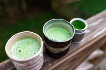 Wooden backyard deck garden railing and two cups with Japanese green tea matcha foam powder in...