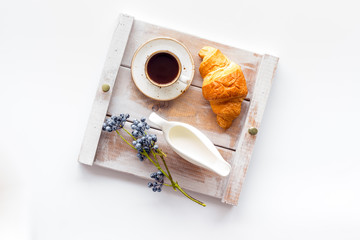 Breakfast in bed with croissant, coffee in cup with milk on tray on white background top view