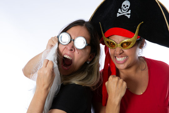 Two happy young women having fun isolated over white backgroung. Friendship concept. One is wearing a white beard and glasses and the other a pirate hat and yellow sunglasses. Happy Halloween party.