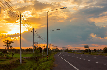 Fototapeta na wymiar Landscape in the fields and background, orange sky, twilight and electric poles on the road