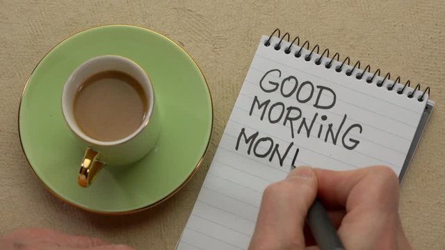 Good Morning Monday - man hand writing a note with a black marker in a spiral notebook, overhead view