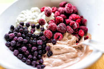 Macro closeup of colorful bowl of vanilla and chocolate ice cream topped with frozen blueberries bilberries and red raspberries berries
