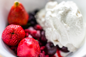 Macro closeup of colorful bowl of vanilla ice cream topped with fresh red strawberry large berries