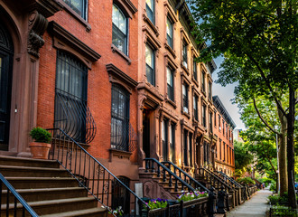 Fototapeta na wymiar Scenic view of a classic Brooklyn brownstone block with a long facade and ornate stoop balustrades on a summer day in Clinton Hills, Brooklyn