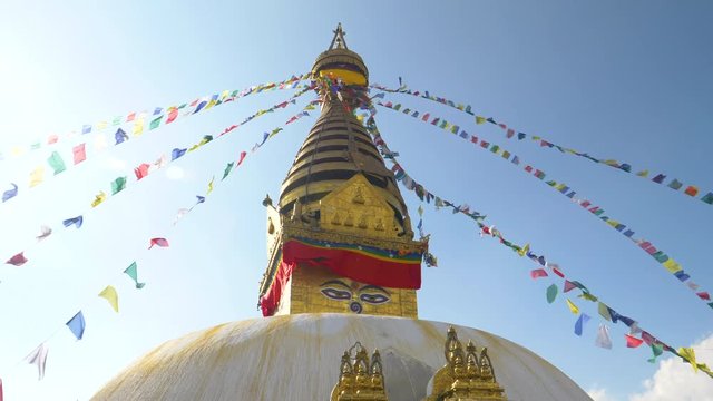 SLOW MOTION, LENS FLARE: Swayambhunath stupa and prayer flags moving in the strong winds blowing in Nepal. Breathtaking view of an ancient hindu temple and colorful ribbons on a sunny day in Kathmandu
