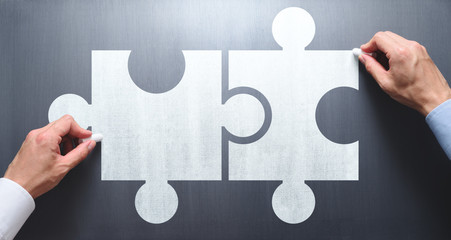 Finding solution of business relationship. Businessmen drawing puzzle pieces on chalkboard.