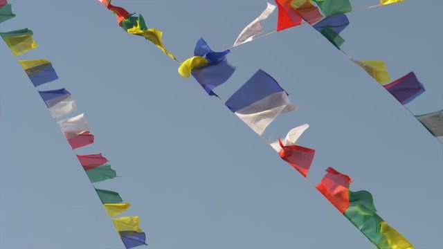 SLOW MOTION CLOSE UP: Multicolored prayer flags hanging off ropes suspended from Monkey Temple flutter in the strong wind blowing across Kathmandu. Beautiful shot of colorful flags in moving in breeze