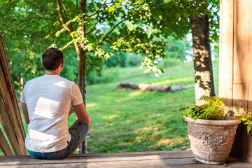 Spring house porch with man sitting on steps of house in front or back yard morning wooden cabin cottage drinking coffee