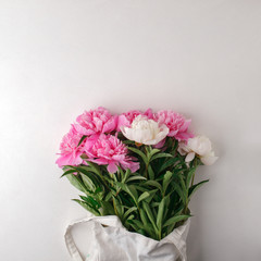 Colorful flowers in organic tissue bag on white table. Space for text. Romance creative layout, blogger lifestyle, minimal festive background