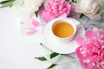 Fototapeta na wymiar Morning cup of herbal tea and colorful flowers on marble plate on white top view. Flat lay style. Creative breakfast for Woman day. Blogger breakfast lifestyle
