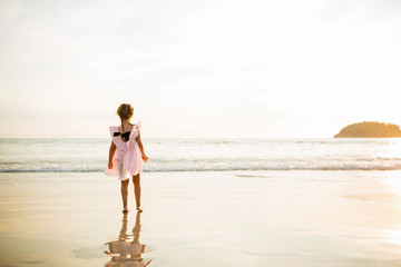 Fototapeta na wymiar Cute little girl walking on the beach. Sunset time. Kid having fun in holiday vacation with back sun light - Youth, lifestyle, travel and happiness concept