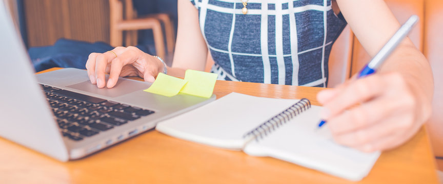Woman hand working at a computer and writing on a notepad with a pen in the office.Web banner.