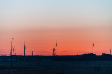 Fototapeta na wymiar Snyder, USA view of wind turbine farm and power lines in Texas countryside industrial town and horizon with colorful red sunset