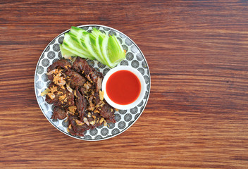 Deep fried beef served with sliced cucumber and sweet chili sauce on wooden board background with copy space.