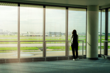 Fototapeta na wymiar a woman travels by airplane standing and waiting at airport terminal for departure flight with windown background and morning sunlight