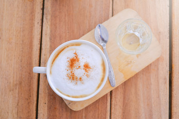 cappucino coffee in white white  cup and drinking water is served on wooden table