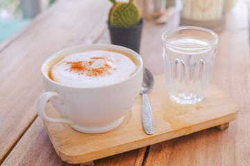 cappucino coffee in white white  cup and drinking water is served on wooden table