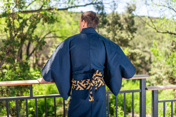 Young man in kimono costume standing back leaning on railing fence in outdoor garden in Japan with...