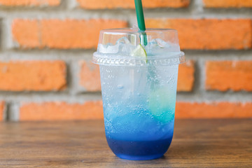 cold blue soda drink with lime slice in take away mug placed on wooden table and brown brick background at cafe 