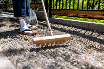 Feet of man in kimono costume and geta tabi shoes socks in outdoor garden raking rock garden in...