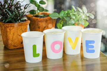 a font wording love on paper mug on table with green plant background for creative decoration corner inside room