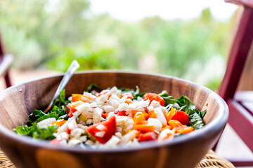 Closeup of fresh salad in wooden bowl with lettuce and bell peppers onions and bokeh background of rocking chair in garden patio