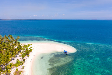 Tropical island of white sand with coconut trees. Boat with tourists on a beautiful beach, aerial view. Seascape, nature of the Philippine Islands.