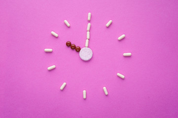 Clock created from white pills and brown tablets on pink background. Right time for using medicines. Brown and white capsules is ten o'clock. Concept: medicine, drugs, healthcare, painkillers, time.