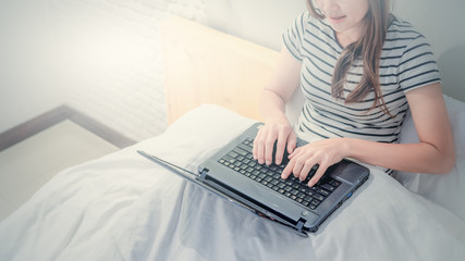 Young asian woman playing with laptop on her bed in white bedroom background.