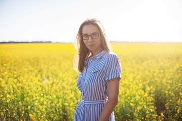 Naklejka na ściany i meble Beautiful woman in field with yellow flowers at summer sunset