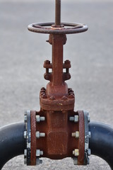 Huge rusty industrial wheel valve bolted to large bore pipes.