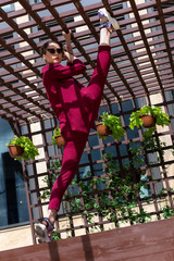 Obraz na płótnie Canvas young girl showing stretching on a city street. Women's trouser suit in red. Female stretching training outdoors. Women's pants and jacket burgundy color.