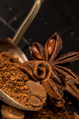 Stick of cinnamon and oriental spices, aniseed cocoa, with a vintage spoon of ground coffee and unroasted grains on a dark background. free space for your text. Close-up macro image.