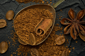 Stick of cinnamon and oriental spices, aniseed cocoa, with a vintage spoon of ground coffee and unroasted grains on a dark background. free space for your text. Close-up macro image.