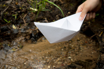 hand of the child launches a paper boat on the river in the spring day