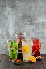 Group of four jugs with lemonades with white and red wine, tropical and berries taste at wooden background.