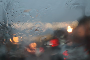Rain drops on glass of car window with street bokeh at evening  in rainy season