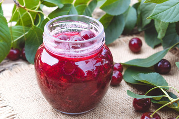 Fresh cherry jelly with fruit on a wooden background near the berries and green leaves.