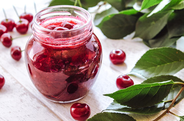Fresh cherry jelly with fruit on a wooden background near the berries and green leaves.
