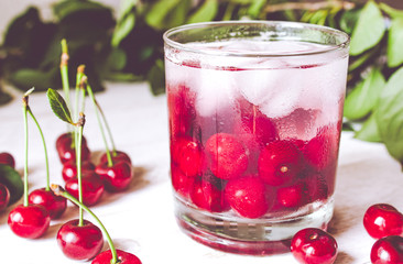 Fresh cherry cocktail with ice on a white wooden background. Fresh summer cocktail with cherries and ice cubes.