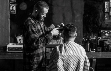 Man visiting hairstylist in barbershop. Bearded man in barbershop. Man hairstylist. Hairdresser cutting hair of male client. Hairstylist serving client at barber shop. Black and white