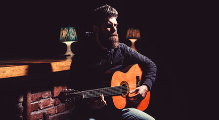 Obraz premium Play the guitar. Beard hipster man sitting in a pub. Bearded man playing guitar, holding an acoustic guitar in his hands. Music concept. Bearded guitarist plays. Copy space.