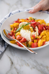 Frau isst Mozzarella Kugel mit roten und gelben Tomaten, Basilikum und Olivenöl auf Teller und  Marmor Hintergrund