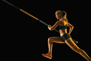 Power and beauty. Professional female pole vaulter training on black studio background in neon...